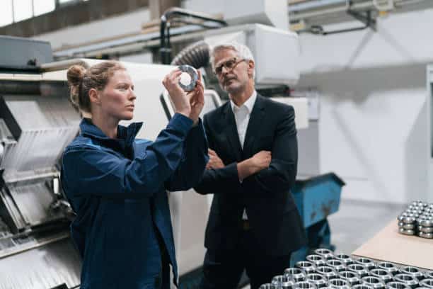 Jeune ouvrière qui examine un produit sous l'oeil d'un cadre